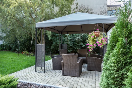Scène extérieure de jardin avec pergola moderne abritant un salon de jardin en résine tressée marron