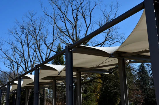 Extérieur jour, pergola moderne avec structure métallique anthracite et toiles tendues blanches créant zones d'ombrage