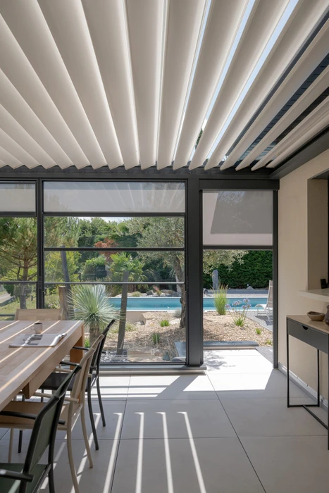 Terrasse couverte par une pergola bioclimatique à lames orientables en aluminium anthracite, adossée à une villa contemporaine
