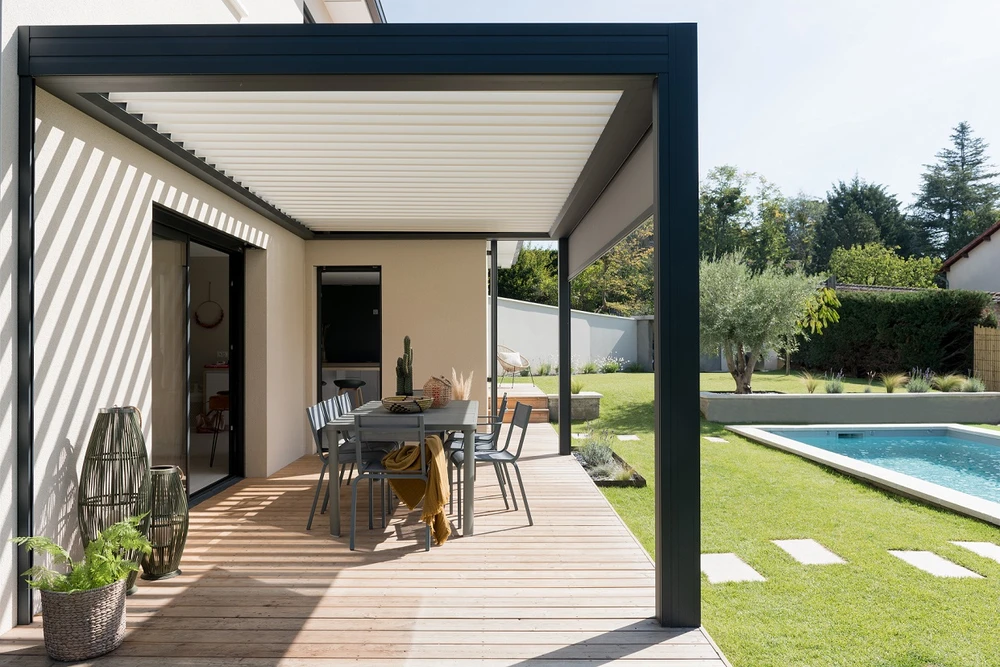 Terrasse couverte par une pergola bioclimatique à lames orientables en aluminium anthracite, adossée à une villa contemporaine