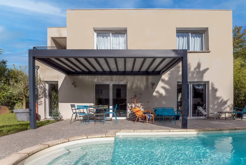 Pergola bioclimatique aluminium anthracite à lames orientables, adossée à une villa contemporaine, terrasse bois composite avec piscine à débordement
