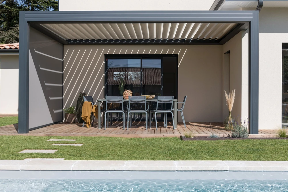 Pergola bioclimatique à lames orientables en aluminium anthracite, structure autoportante fixée en façade d'une maison contemporaine