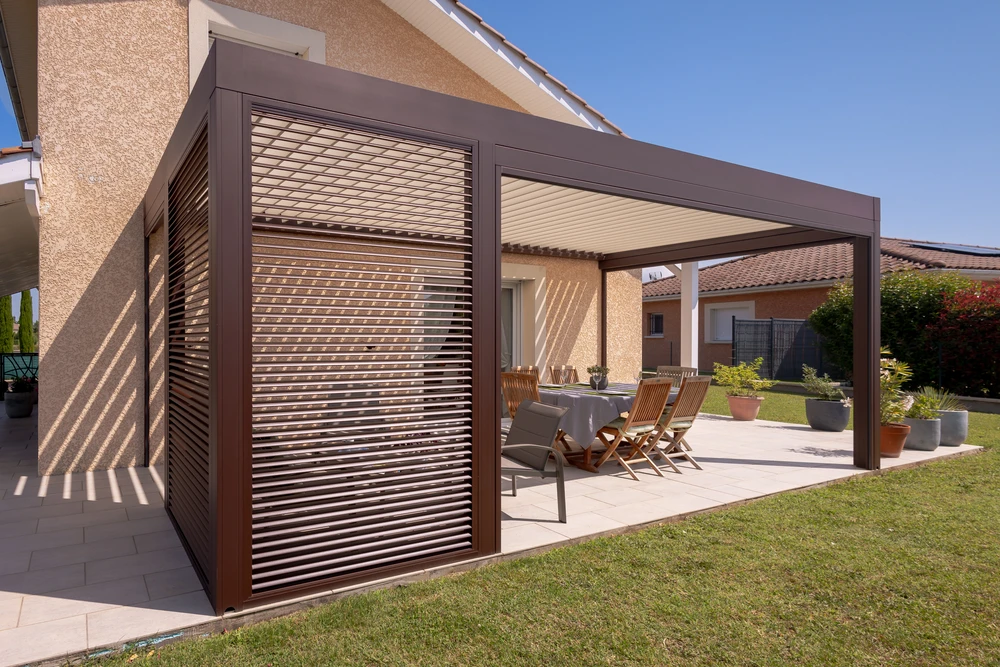 Pergola bioclimatique à lames orientables en aluminium anthracite, structure autoportante fixée en façade d'une maison contemporaine